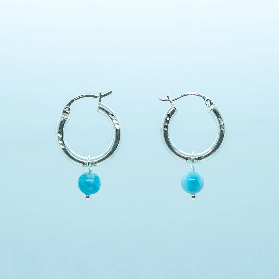 Photo d'une paire de boucles d'oreilles créoles vue de face sur fond blanc. Créoles en argent 925 avec une perle de larimar de République Dominicaine en pendant.