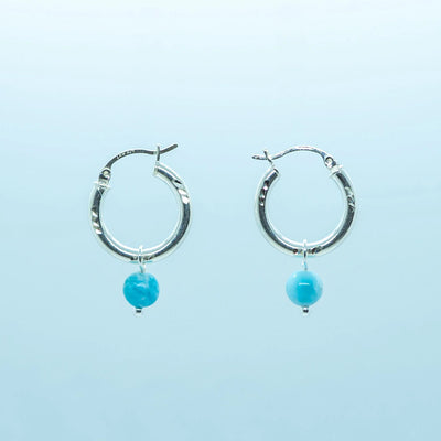 Photo d'une paire de boucles d'oreilles créoles vue de face sur fond blanc. Créoles en argent 925 avec une perle de larimar de République Dominicaine en pendant.