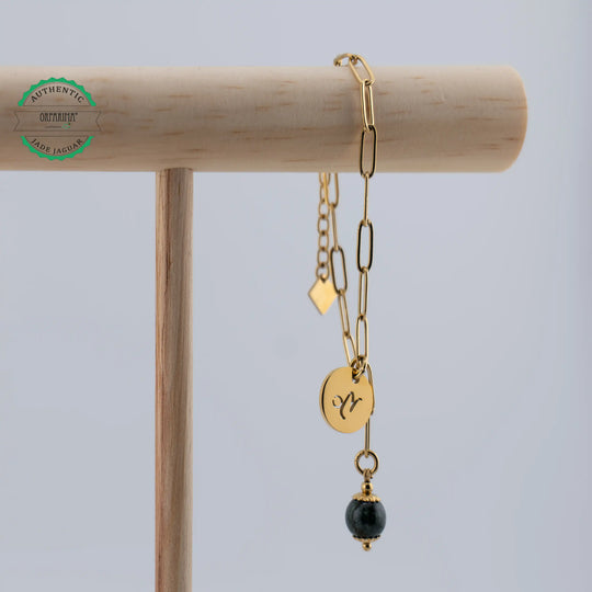 Bracelet en acier inoxydable doré suspendu à un présentoir en bois. Bijou fait artisanalement en République Dominicaine avec une perle de Jade Jaguar vert foncée venant du Guatemala.