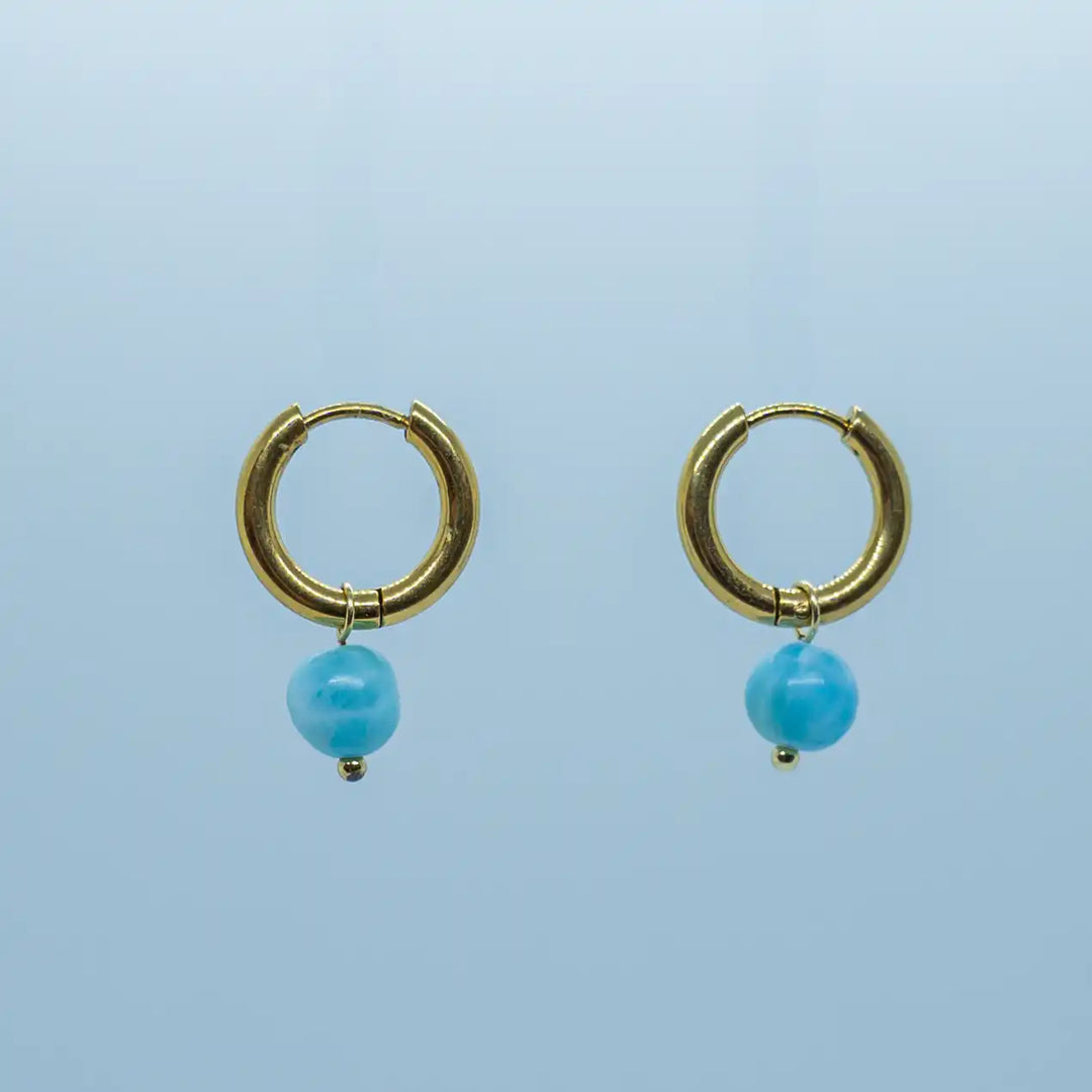 Paire de créoles dorées montées avec une perle de Larimar de couleur bleu. Bijoux en acier inoxydable 316L avec un plaquage PVD doré.