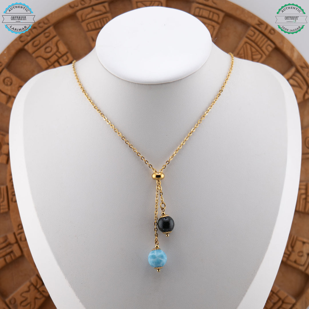 Deux perles naturelles, la première en Jade Jaguar et la deuxième en Larimar, sont montées sur un collier doré avec une bague en caoutchouc permettant de régler la position de chacune des perles.