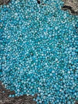 plusieurs centaines de perles de Larimar de différents diamètres exposées dans un linge gris. Perles en pierre naturelle de Larimar de République Dominicaine à la couleur bleu unique.