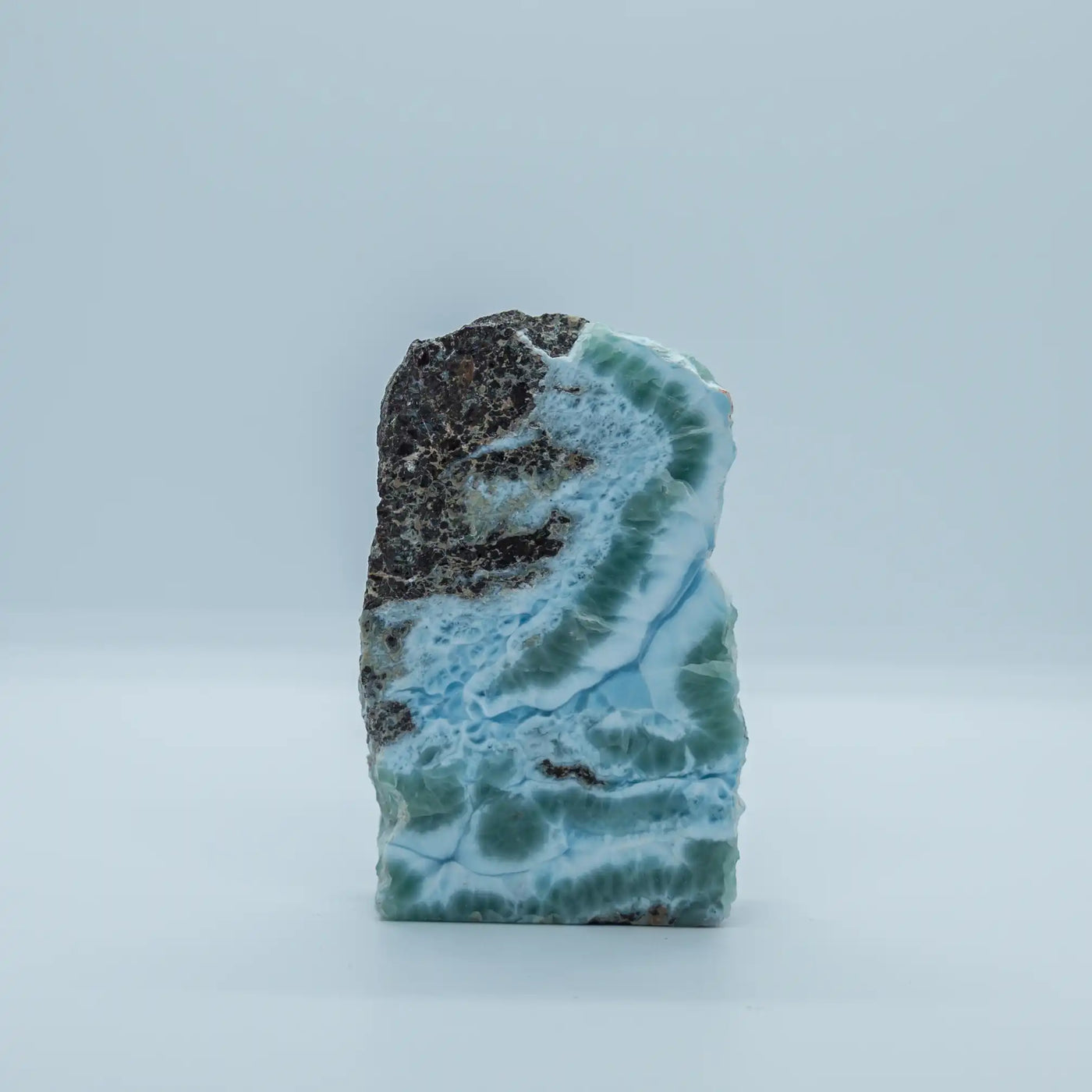 Petit bloc de Larimar venant de République Dominicaine, prit en photo de face. Cette roche possède plusieurs nuance de couleurs dont la principale est le bleu, mais du vert et du blanc sont également présent sur ce bloc, ainsi qu'une partie rocheuse sur la partie en haut à gauche.