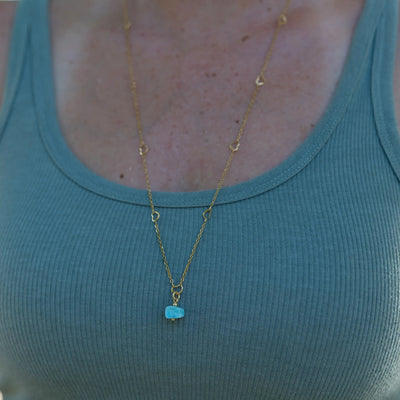 Photo prise en macro d'un sautoir en acier inoxydable de couleur doré. Ce sautoir à un pendentif en pierre naturelle de Larimar de couleur bleue. bijou créé artisanalement en République Dominicaine.