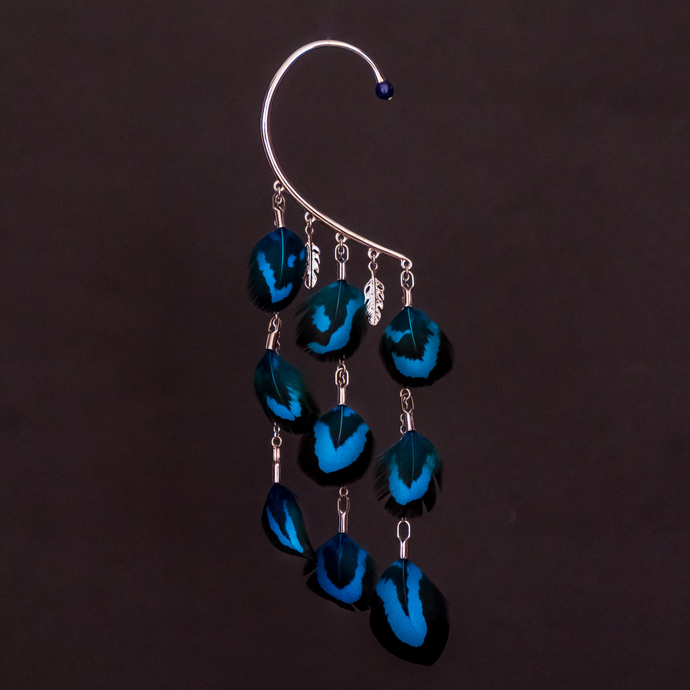 Tour d'oreille faisan electrik de couleur bleue, bijou qui se pose sur l'oreille droite, bijou original et chic. Bijou seul sur fond noir, trois pendants ornés de plume bleues et deux petits après en forme de plume doréau palladium.