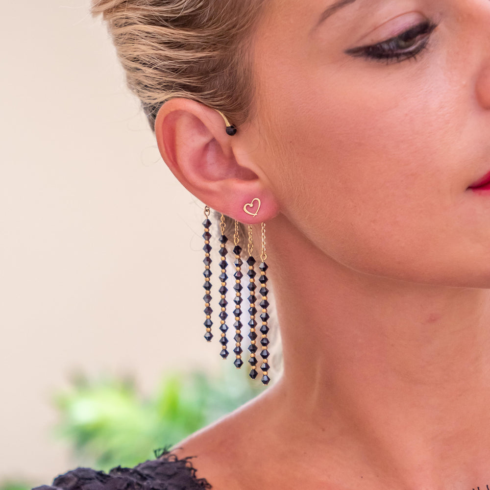 Bijou d'oreille fait en laiton plaqué or avec cinq pendants ornés de cristaux de Swarovski noirs. Ce bijou est porté par un femme blonde, la photo est centrée sur l'oreille.