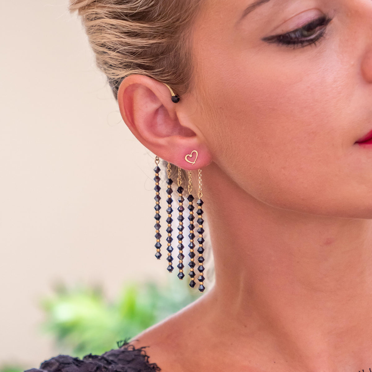 Bijou d'oreille fait en laiton plaqué or avec cinq pendants ornés de cristaux de Swarovski noirs. Ce bijou est porté par un femme blonde, la photo est centrée sur l'oreille.