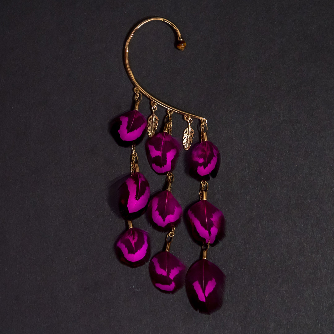 Tour d'oreille Orparima est ses plumes de faisan vénéré de couleur fushia. Bijou avec une petite perle d'énergie oeil de tigre, doré à l'or fin 24 carats et se portant sur l'oreille droite.