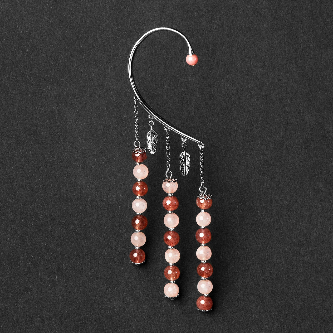 Orparima Tour d'oreille modèle "Amour" de la Collection Energie, en vue serré sur fond noir. Bijou orné d'une perle de Rhodonite sur le devant, doré au Palladium.