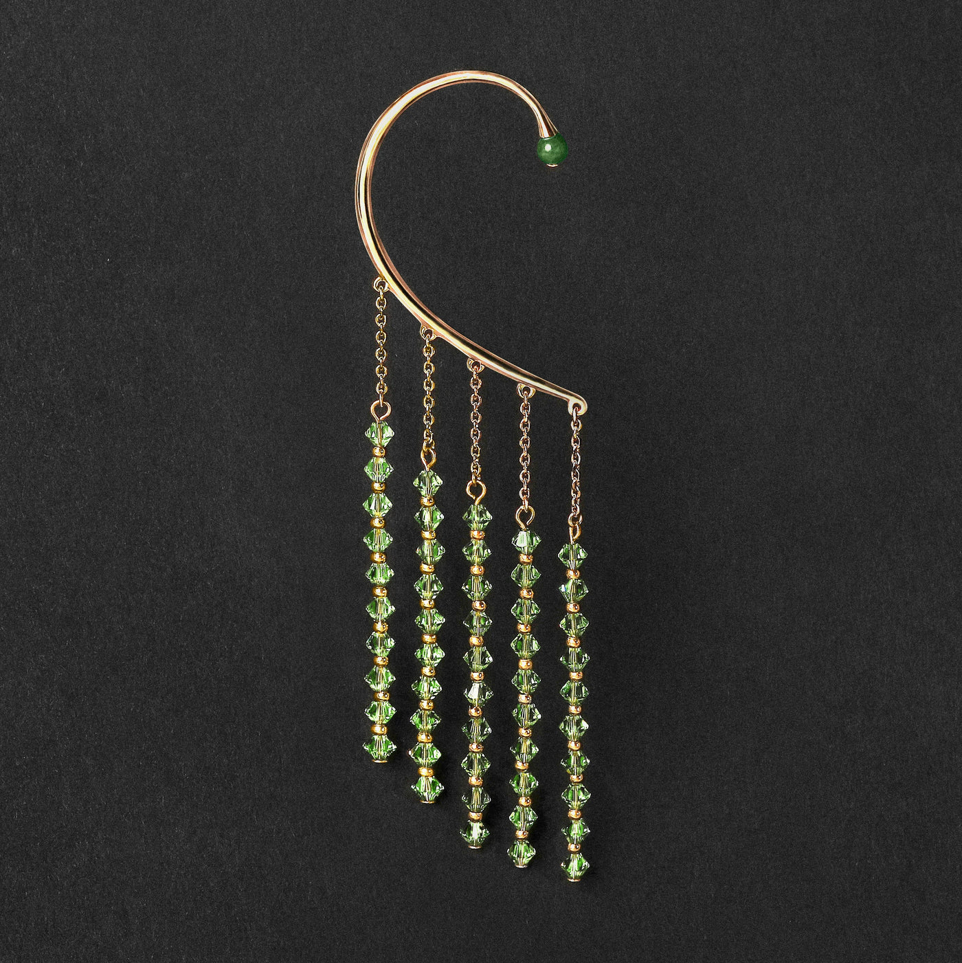 Orparima Tour d'oreille modèle "Green Diamond", de la Collection Swarovski, sur fond noir. Bijou doré à l'or fin 24 Carats et orné d'une perle de Jade d'Afrique sur le devant.
